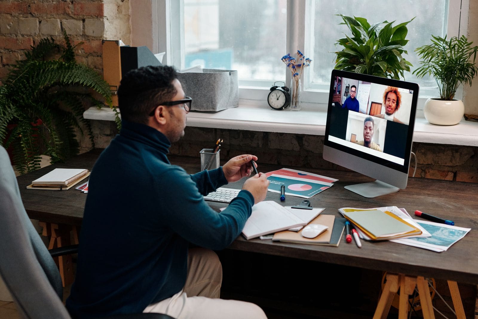A teacher on a video call with students, speaking to a laptop at a desk