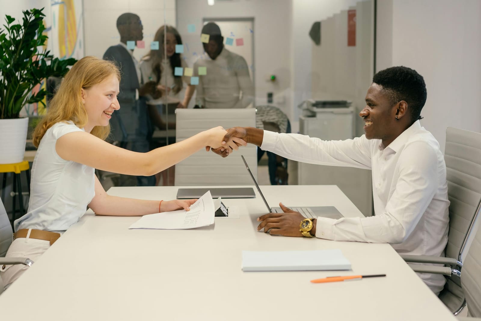 Two business professionals shaking hands across a desk in a modern office